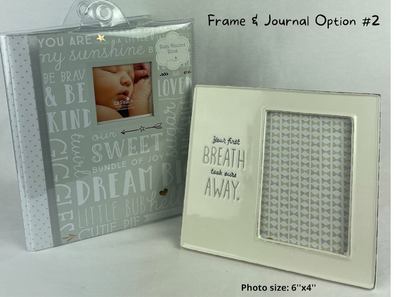 May include: A white ceramic frame with a gray and white patterned background. The frame has a cutout for a 6x4 inch photo and the text "Your first breath took ours away." The frame is next to a gray journal with the text "You are a little sunshine" and other positive words.