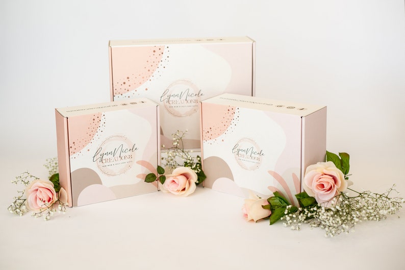 May include: Three pink and white gift boxes with a gold and white abstract design. The boxes have the text "Lynn Nicole Creations" on them. The boxes are surrounded by pink roses and white baby's breath.