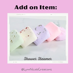 May include: Five different colored shower steamers, arranged in a row on a white marble surface. The steamers are square shaped and have a variety of dried flowers and herbs embedded in them. The text "Shower Steamer" is visible below the steamers, and the text "@LynnNicoleCreations" is visible below that.