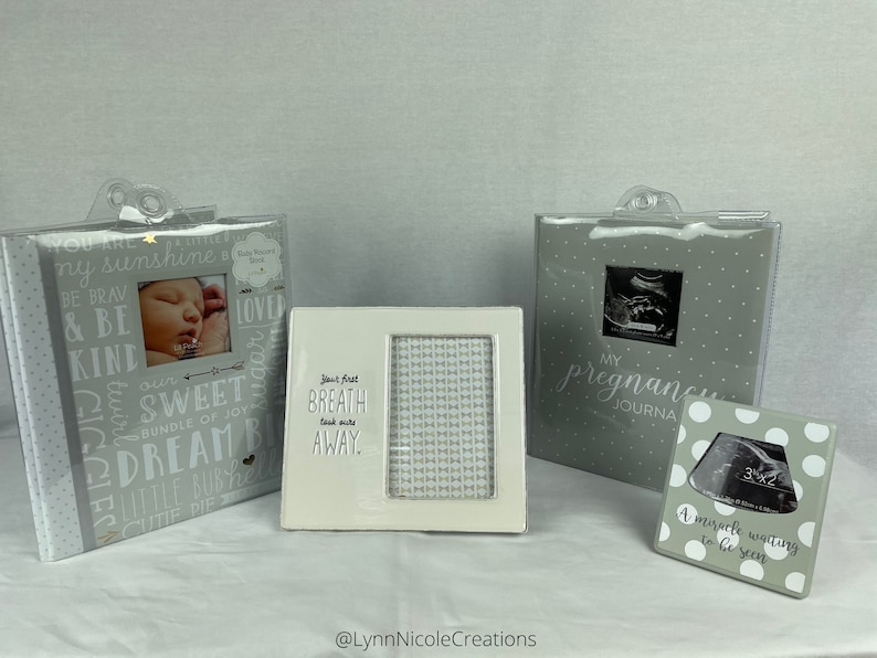 May include: Three gray photo albums with white polka dots and silver accents. The albums are for baby memories, pregnancy, and ultrasound photos. The text on the albums reads "You are my sunshine", "My Pregnancy Journal", and "A miracle waiting to be seen".
