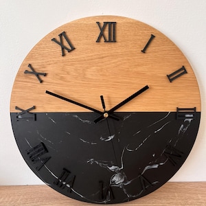 Puede incluir: Un reloj de pared redondo con un diseño de dos tonos. La mitad superior es de madera marrón claro y la mitad inferior es de mármol negro. Los números romanos negros marcan las horas y las manecillas negras indican la hora. El reloj mide unos 30 cm de diámetro.