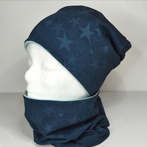Könnte beinhalten: Ein Set aus einer dunkelblauen Mütze und einem passenden Schlauchschal mit einem sich wiederholenden Sternenmuster in einem etwas helleren Blauton. Beide Teile sind mit einem hellen mintgrünen Stoff gefüttert, der an den Rändern sichtbar ist.