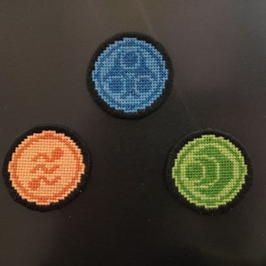 Puede incluir: Tres parches redondos bordados con diferentes diseños. El primer parche es azul con un diseño circular, el segundo es naranja con un diseño ondulado y el tercero es verde con un diseño circular.