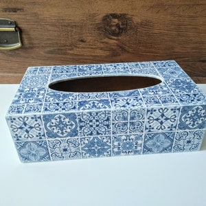 Puede incluir: Caja de pañuelos rectangular con un patrón de azulejos azules y blancos. La caja tiene un interior marrón y una abertura rectangular para dispensar pañuelos. El diseño presenta un patrón repetitivo de formas florales y geométricas.