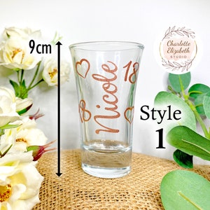 May include: A clear glass shot glass with a copper-colored design that says "Nicole 18" with hearts. The shot glass is 9 cm tall. Style 1.