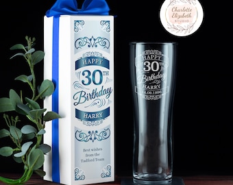 May include: A clear glass beer pint glass and a tall white gift box with a blue ribbon. The glass and box feature blue decorative scrollwork and text reading Happy 30th Birthday Harry 14.09.1996. The box also includes Best wishes from the Tadford Team.