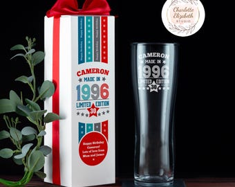 May include: A clear glass beer pint glass and a tall white gift box with a red ribbon bow. The glass and box feature white, red, and blue text reading Cameron Made In 1996 Limited Edition 30, with stars and a circular message from Mum and James.