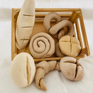 Könnte beinhalten: Eine Holzkiste gefüllt mit verschiedenen Brotsorten, darunter ein Baguette, ein Brezel, ein Croissant und ein paar Brötchen. Das Brot ist alles aus Teig und hat eine hellbraune Farbe.