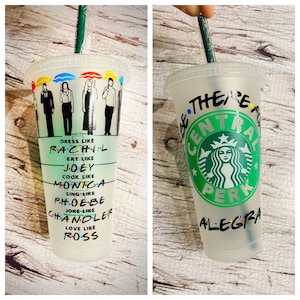May include: Two clear plastic cups with lids and straws. One cup has a design of the Friends characters and text that says "Dress like Rachel, Eat like Joey, Cook like Monica, Sing like Phoebe, Joke like Chandler, Love like Ross". The other cup has a green Starbucks logo with the text "Be there for Central Perk" and the name "Alegria".