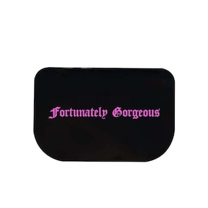 Può includere: Palette per il trucco rettangolare nera con il testo "Fortunately Gorgeous" in lettere rosa.