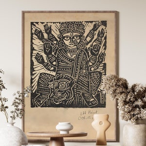 May include: A black and white print of a Hindu deity with multiple arms, framed in a light brown frame. The print is displayed on a wooden shelf with two white ceramic vases, a wooden pedestal, and a small white ceramic bowl. The print is titled "1st Print Oct. 12, 1974".