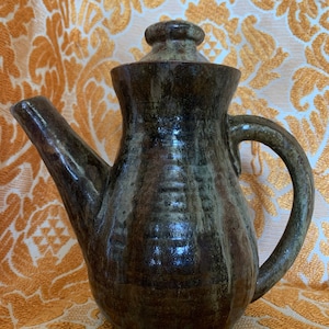 May include: A dark green and brown ceramic teapot with a lid. The teapot has a textured, hand-thrown look.