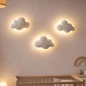 Könnte beinhalten: Ein Kinderzimmer mit einem Holzbett, einer Wickelkommode und drei wolkenförmigen Wandleuchten. Der Raum ist in neutralen Tönen gehalten, mit einer gewebten Pendelleuchte und einem Bücherregal aus Holz. Ein kleiner Tisch mit einer Lampe steht neben dem Bett.