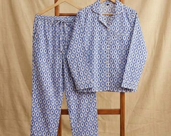 Könnte beinhalten: Blau-weiß gemustertes Pyjama-Set, bestehend aus einem Hemd mit Knöpfen und einer Hose mit Kordelzug, präsentiert auf einem hölzernen Kleiderbügel und Ständer. Die Nachtwäsche hat ein sich wiederholendes ovales Design und weiße Paspeln.