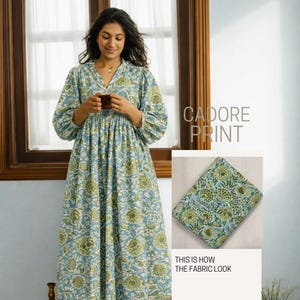 May include: A long-sleeved dress featuring a light blue and green floral pattern labeled Cadore Print. The dress has a V-neckline and a gathered waist. An inset shows a folded piece of the same floral fabric with the text This is how the fabric look.