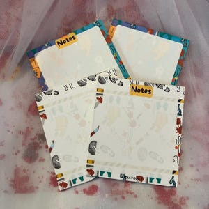 May include: Three colorful patterned notepads with the word "Notes" printed on each. The notepads have a white background with colorful illustrations of footprints, animals, and other designs.