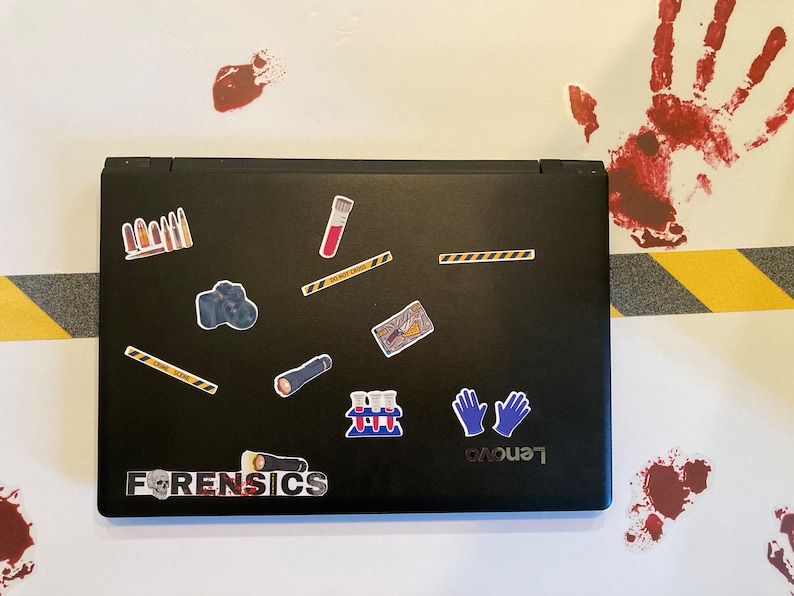 May include: A black laptop with various stickers on the lid, including a camera, a torch, a test tube, a pair of blue gloves, and the word "FORENSICS". The laptop is on a white surface with yellow and black caution tape and red handprints.