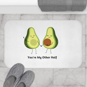 May include: White bath mat with a graphic of two avocado halves holding hands. The avocado halves have smiling faces and the text "You're My Other Half" is printed below the avocados.