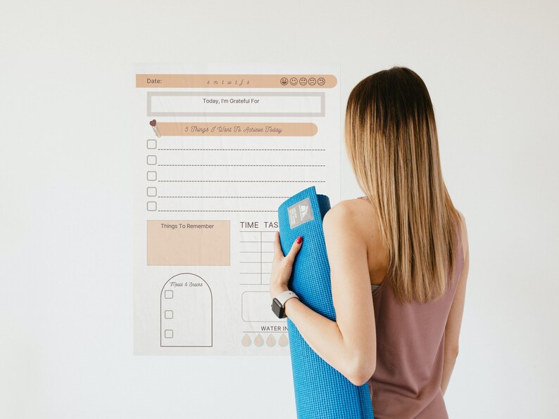 May include: A white printable planner with a brown header and a section for daily gratitude, things to remember, time tasks, and water intake. The planner is on a white wall with a woman holding a blue yoga mat.