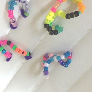 May include: Four colorful beaded bracelets with fuzzy ends. The bracelets are made with small, round beads in various colors, including pink, blue, green, yellow, orange, and black.