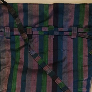 Puede incluir: Un bolso de mano de tela a rayas con una correa larga. El bolso está hecho de tela tejida con rayas azules, verdes, moradas y negras.