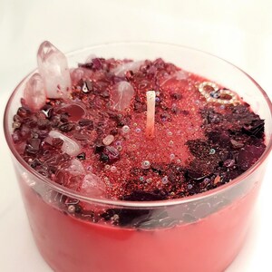 Peut inclure: Une bougie rouge dans un pot en verre transparent, incrustée de petits cristaux et de paillettes. La bougie a une seule mèche et est entourée d'une bordure décorative rouge et noire.