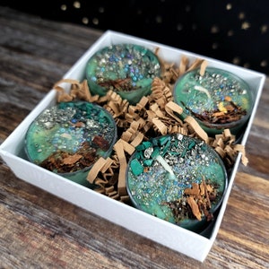 May include: Four teal green tea light candles with embedded crystals and glitter in a white gift box with brown shredded paper.