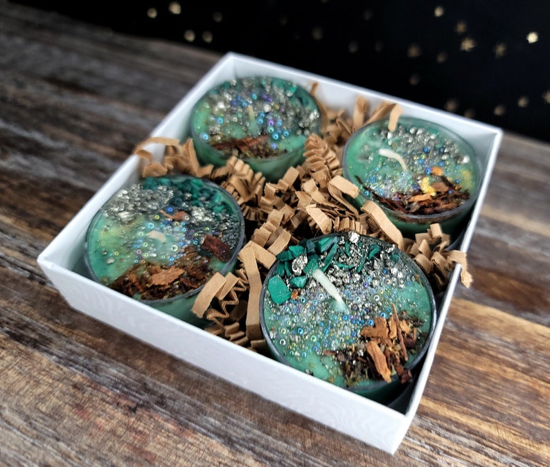 May include: Four teal green tea light candles with embedded crystals and glitter in a white gift box with brown shredded paper.