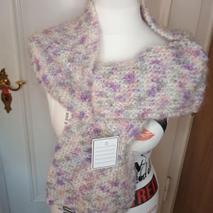 Könnte beinhalten: Ein weicher, weißer, lila und blauer Strick Schal mit einem weißen Etikett. Der Schal ist über eine weiße Schaufensterpuppe gelegt.