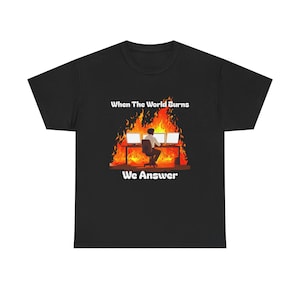 Pode incluir: Camiseta preta com um gráfico de uma pessoa sentada em frente a várias telas de computador com chamas atrás. O texto "When The World Burns We Answer" está impresso na camiseta.