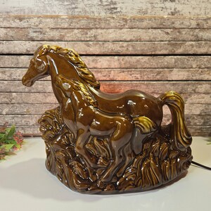 May include: A brown ceramic lamp shaped like a mother horse and her foal. The lamp is in a rustic style and has a brown and green glaze.