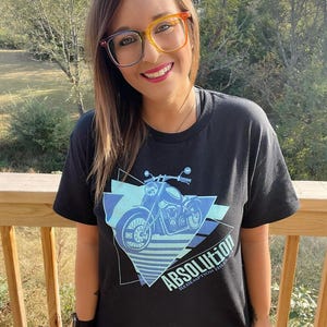 May include: Black t-shirt with a blue and white graphic of a motorcycle and the text "ABSOLUTION REDEMPTION THRIVE".