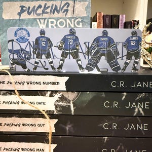 Puede incluir: Un marcapáginas con jugadores de hockey con uniformes azules, con el texto "DALLAS KNIGHTS" y nombres de jugadores. El marcapáginas está sobre una pila de libros con los títulos "THE PUCKING WRONG NUMBER", "DATE", "GUY" y "MAN".