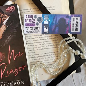 Puede incluir: Una composición que presenta un libro, una entrada de concierto y un collar de perlas. La entrada es para "A Riot of Roses" con el texto "Meet and Greet to Follow Music." La portada del libro muestra el título "Me Reason" de Jackson.