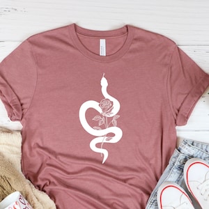 Könnte beinhalten: Ein mauvefarbenes T-Shirt mit einer weißen Grafik einer Schlange, die sich um eine Rose windet.