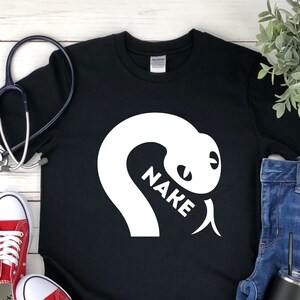 Pode incluir: Camiseta preta com um gráfico de cobra branca e a palavra "NAKE" escrita dentro do corpo da cobra.
