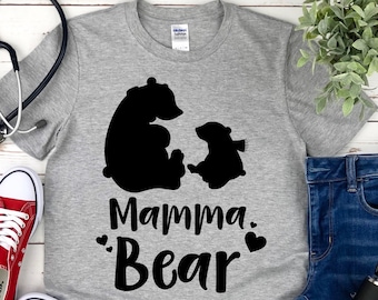 Puede incluir: Camiseta gris con una silueta negra de una osa madre y un osezno. El texto "Mamma Bear" está impreso debajo de los osos con dos pequeños corazones.