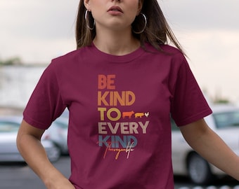 May include: A maroon t-shirt with a vintage-style graphic that reads "Be Kind To Every Kind of Life". The graphic features a rainbow colour scheme and includes a row of farm animals.