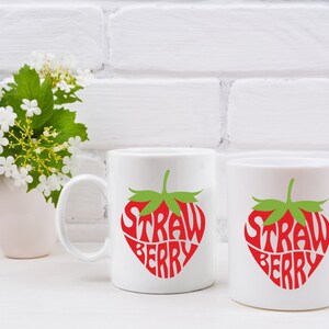 May include: Two white ceramic mugs with a red and green strawberry design. The text "Strawberry" is written inside the strawberry shape.