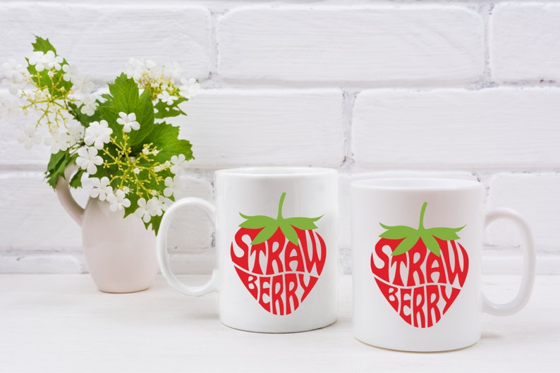 May include: Two white ceramic mugs with a red and green strawberry design. The text "Strawberry" is written inside the strawberry shape.
