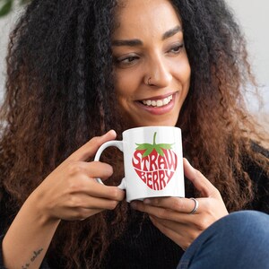 May include: A white ceramic mug with a red strawberry design. The text "Strawberry" is written inside the strawberry shape.