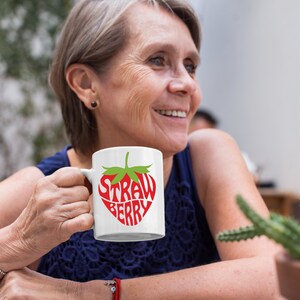 May include: A white ceramic mug with a red and green strawberry design. The strawberry is made up of the words "Straw" and "Berry".