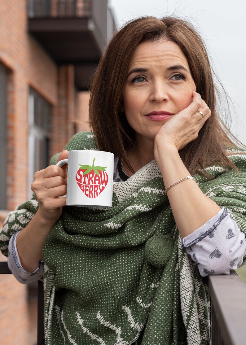 May include: A white ceramic mug with a red strawberry design. The word "Strawberry" is written in a stylized font inside the strawberry shape.