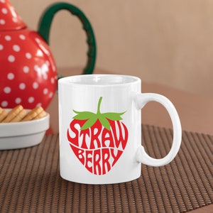 May include: White ceramic mug with a red and green strawberry design. The strawberry is made up of the words "STRAWBERRY" in a stylized font.
