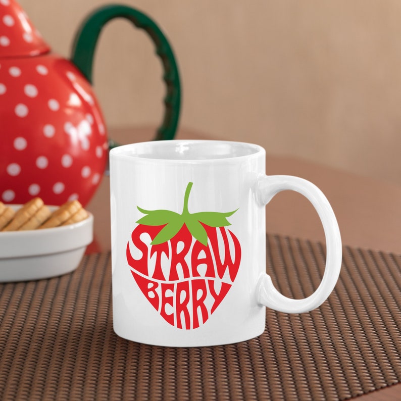 May include: White ceramic mug with a red and green strawberry design. The strawberry is made up of the words "STRAWBERRY" in a stylized font.