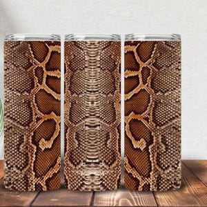 May include: A cylindrical tumbler featuring a repeating brown and tan snakeskin pattern. The design displays a detailed reptilian scale texture across the entire surface, with a metallic rim at the top and a smooth, straight-sided body shape.