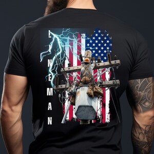 May include: Black t-shirt with a graphic of a lineman working on a power pole in front of an American flag with lightning bolts. The text "LINEMAN" is printed vertically on the left side of the graphic.