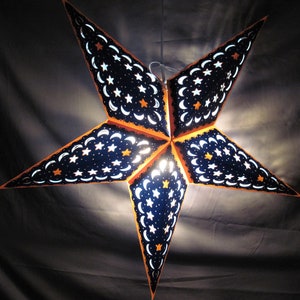 May include: A blue and orange paper star lantern with a crescent moon and star pattern. The lantern is lit from the inside, creating a warm glow.