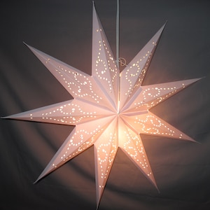 May include: A white paper star lantern with a delicate, intricate design. The star is illuminated from within, creating a warm glow.