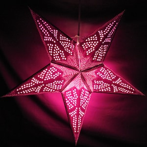 May include: A pink paper star lantern with a white polka dot pattern. The lantern is lit from within, casting a warm glow.